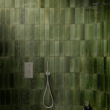 Minimalist shower with green tiled walls and a sleek silver showerhead.