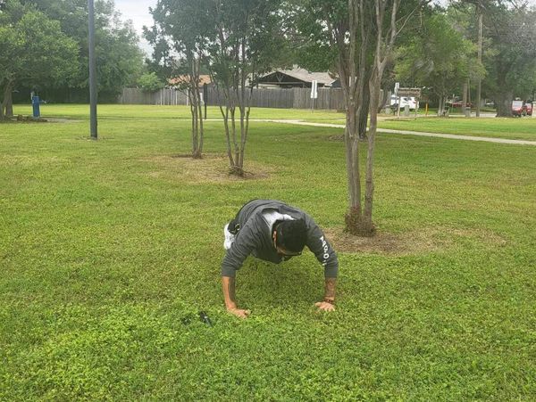 Person doing push-ups on grass in a park-like area.