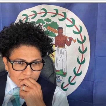 Person with glasses in front of a Belize flag.