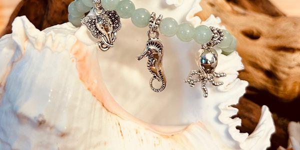 A sea-themed charm bracelet displayed on a white seashell.