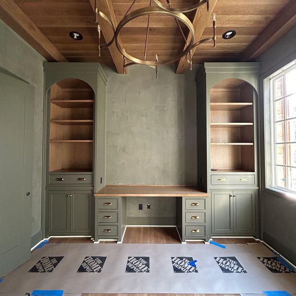 Elegant built-in desk with green cabinetry and wooden shelves under a wooden ceiling.