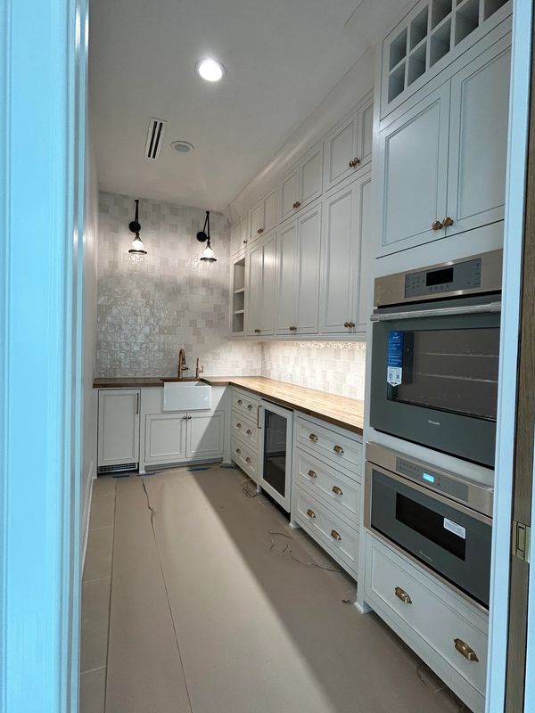 Narrow modern kitchen with white cabinetry, wooden countertops, and built-in appliances.
