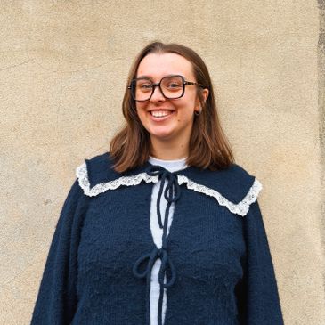 Woman smiling wearing glasses and a navy blue sweater with lace collar.