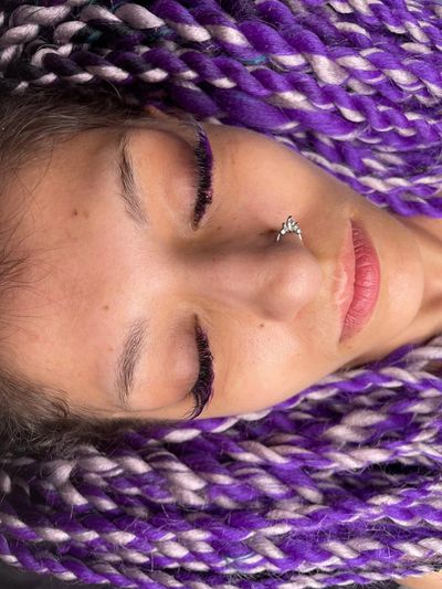 Close-up of a person with purple and white braids, purple eyelashes, and a nose ring.
