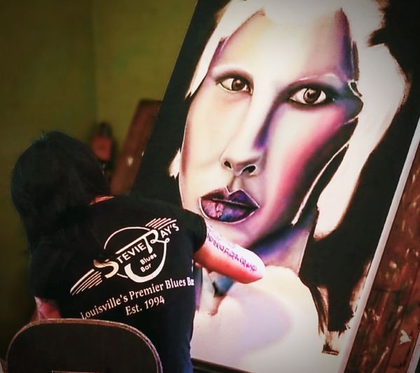 Artist painting a large, expressive portrait of a face.
