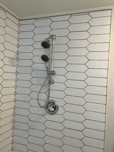 Modern shower with hexagonal white tiles and dual showerheads.