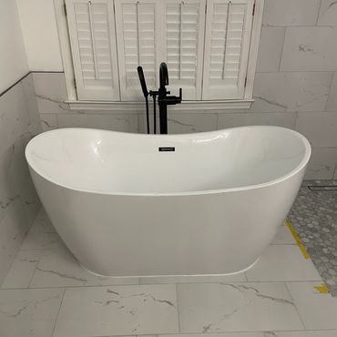 Modern white freestanding bathtub with black faucet in a bathroom.