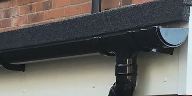 Close-up of a black gutter and downpipe on a brick building.
