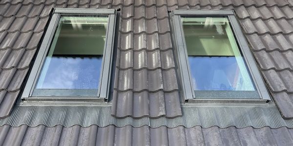 Two skylight windows on a tiled roof reflecting the sky.