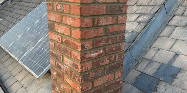 Red brick chimney on a tiled roof with solar panels.