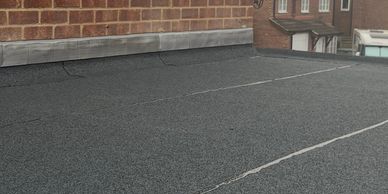 Flat roof with black waterproofing material and brick walls.