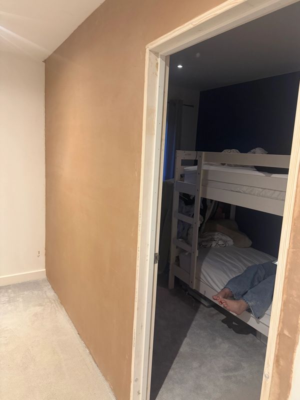 View through an open doorway into a bunk bed room with someone sitting on the lower bed.