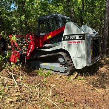 A Takeuchi tracked mini loader working in a forest clearing.
