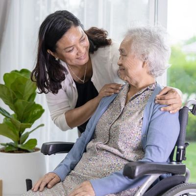 A woman warmly caring for an elderly lady in a wheelchair indoors.