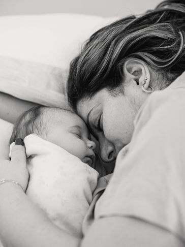 Black and white photo of a woman and an infant laying down, their foreheads touching.