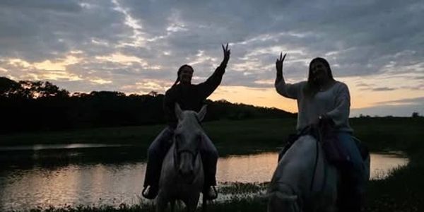 Two riders on white rescue horses enjoying a Texas sunset by the pond at Chisholm Trail Rides near R