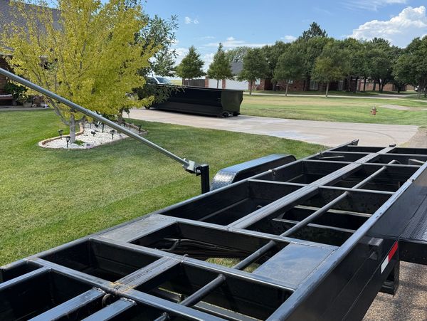 A black metal trailer frame in a suburban driveway under a blue sky.