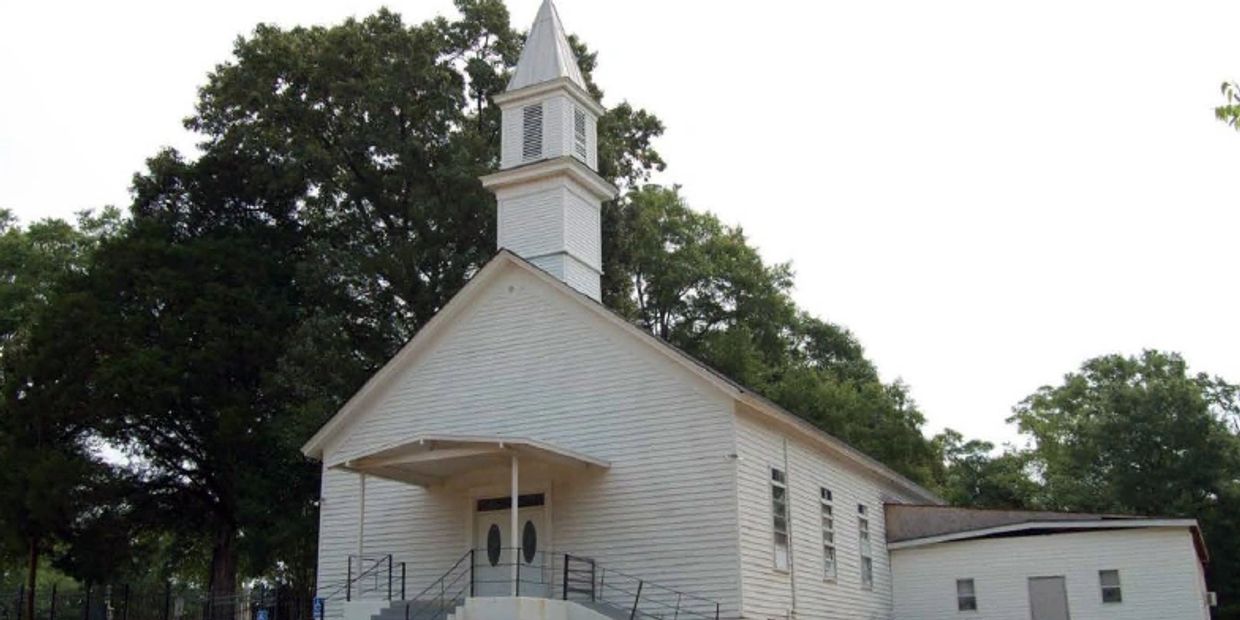 A white wooden church with a steeple and surrounding trees.