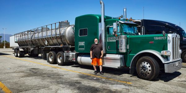Man standing next to a green semi-truck and trailer.