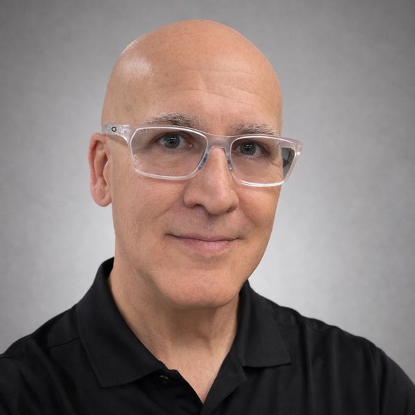 Smiling bald man wearing clear glasses and a black Nike polo shirt.