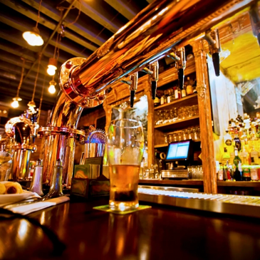 A warm, inviting bar with shiny beer taps and a glass of beer on the counter.