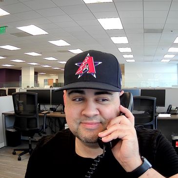 Man wearing a baseball cap talking on a phone in an office.