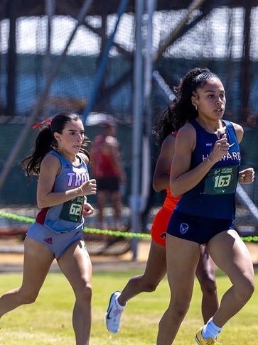 Two female athletes running on a track field.