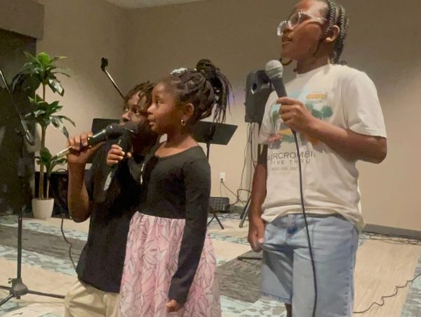Three children holding microphones, performing indoors.