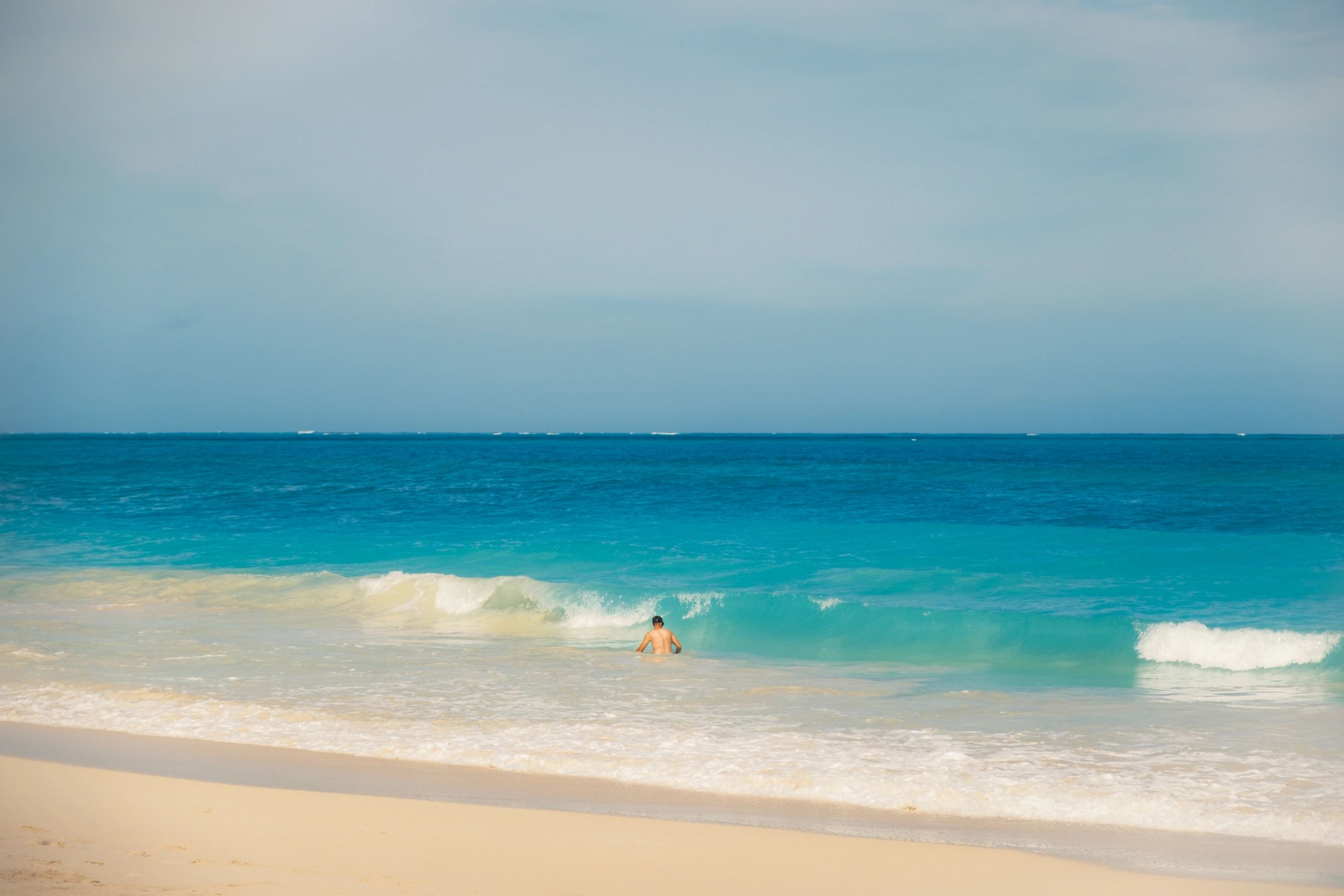 Man wading into the ocean on a sunny beach.