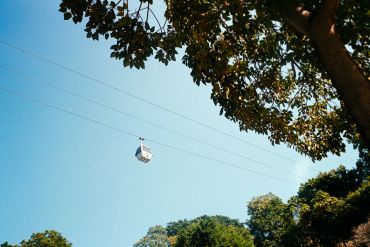 Cable car suspended over trees against a clear blue sky.