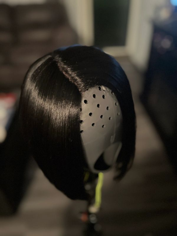 Shiny black wig on a gray mannequin head.