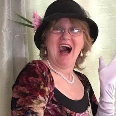 Woman in vintage attire laughing joyfully with a hat and gloves.
