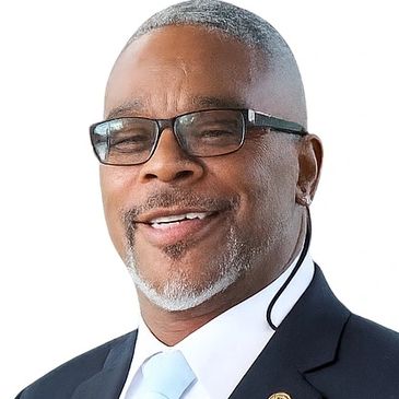 A smiling man wearing glasses and a suit with a light blue tie.