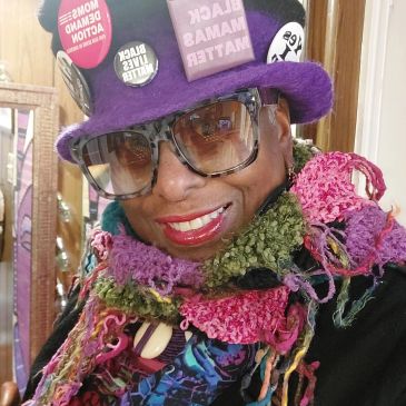 Person wearing a colorful scarf and purple hat with social justice pins.