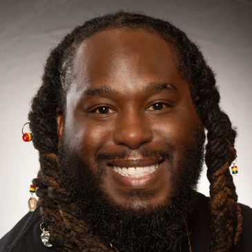 Smiling man with braided hair and colorful beads.