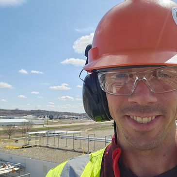 Construction worker smiling with safety gear outdoors on a sunny day.