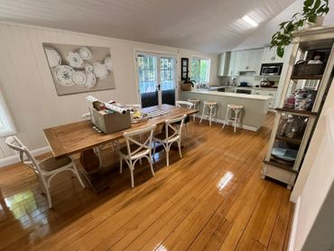 Cozy dining area with wooden table and white chairs next to a modern kitchen with bar stools.