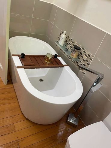 Modern white bathtub with wooden tray and bath essentials in a tiled bathroom.