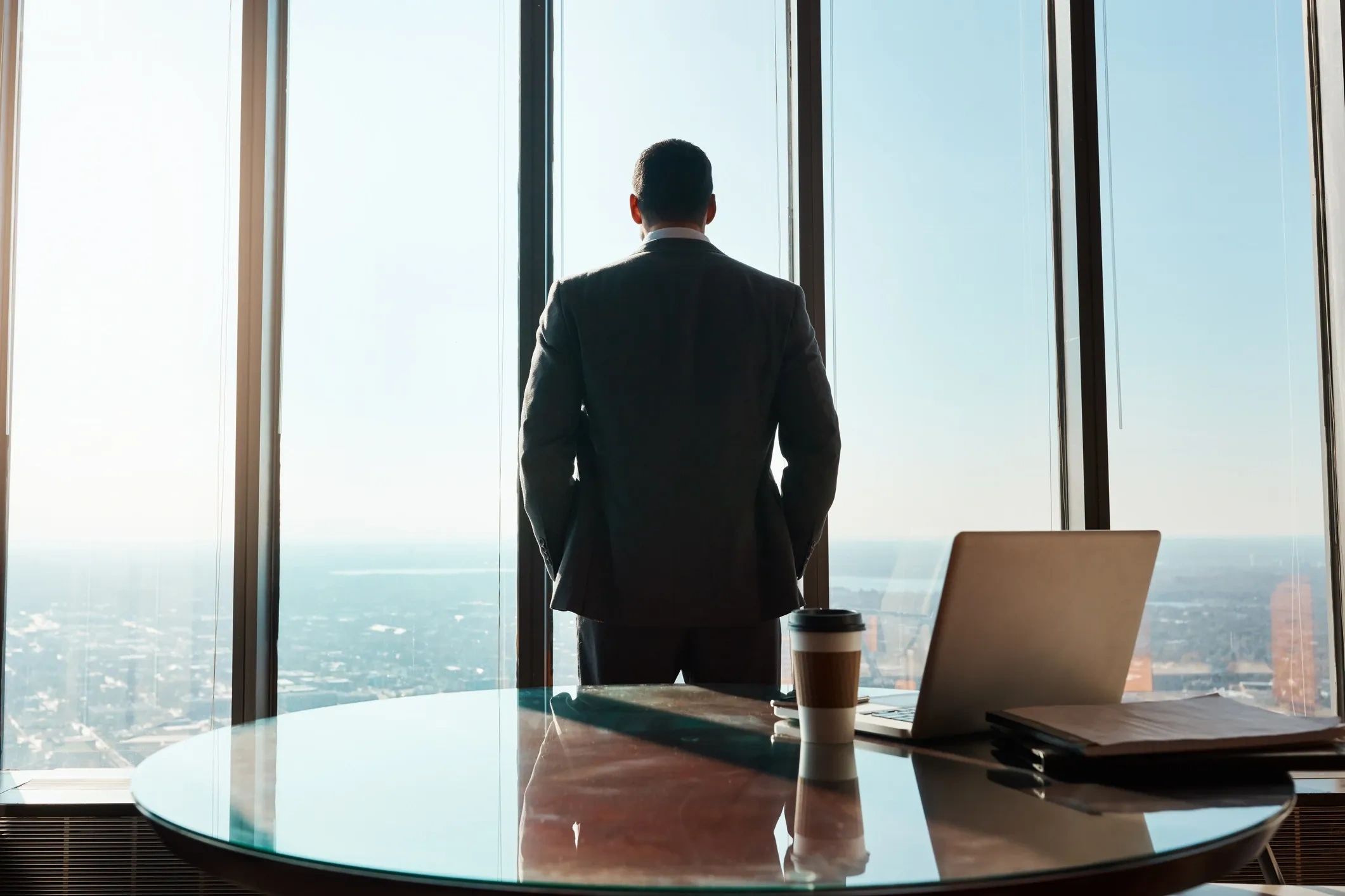Man in suit looking out office window over cityscape.
