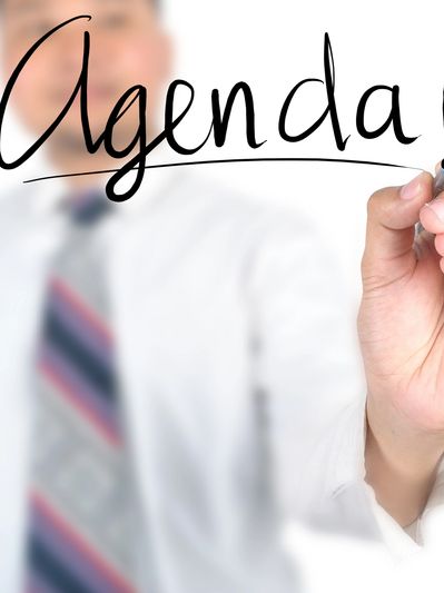 Man writing 'Agenda' on transparent board.
