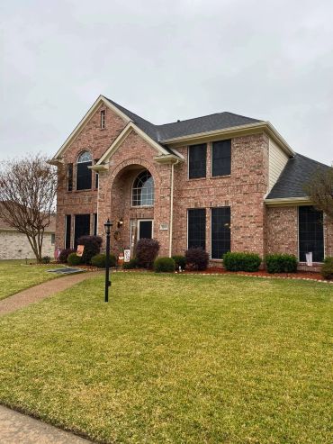 A large brick two-story house with a well-kept lawn and bushes.