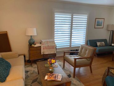 Cozy living room with mid-century furniture and natural light from shuttered windows.