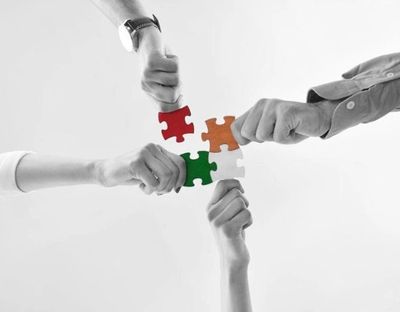 Four hands holding colorful puzzle pieces fitting together symbolizing teamwork.