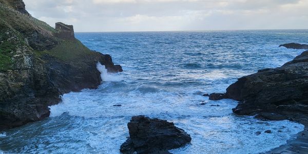 Rocky coastline with waves crashing against cliffs under a cloudy sky.