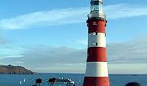 Red and white striped lighthouse by the sea under a clear blue sky.