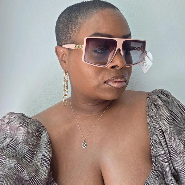 Woman with short hair wearing large pink sunglasses and gold chain earrings.