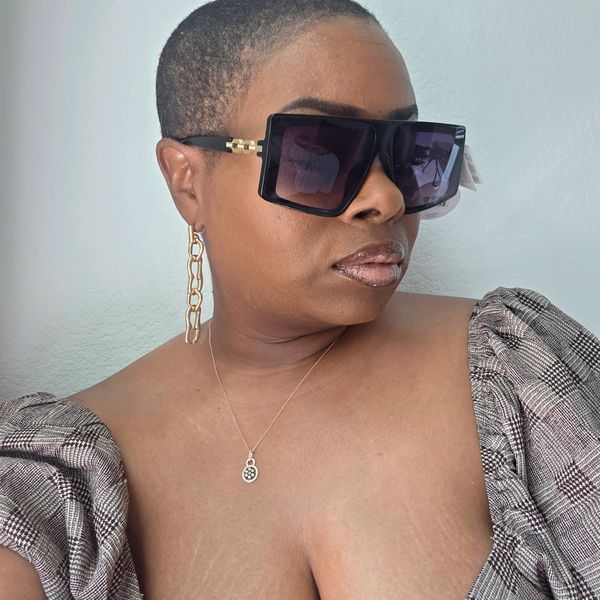 Woman with short hair wearing oversized sunglasses and gold chain earrings.