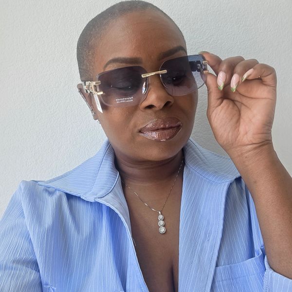 Woman in blue shirt adjusting her sunglasses with a confident expression.