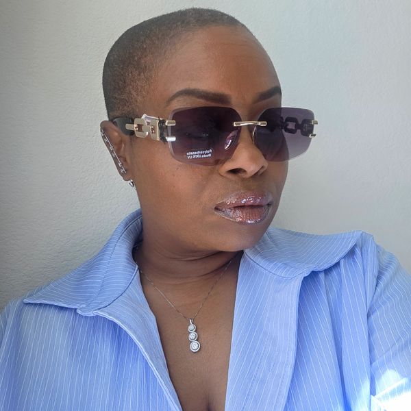 Woman with stylish sunglasses and glittery lips wearing a light blue shirt.