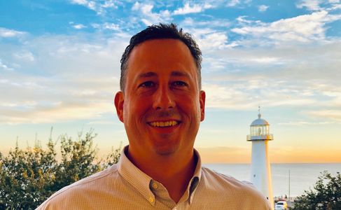 Man smiling in front of a lighthouse during sunset.